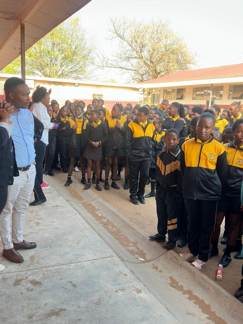 Learners in school uniform gathered in a schoolyard listening to a speaker