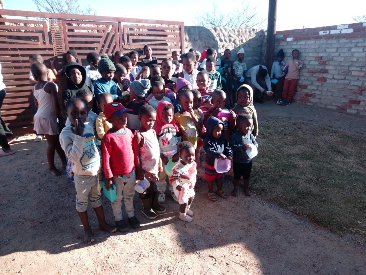 Children holding bowls and cups after receiving a meal at an outreach